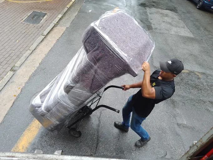 Funcionário da NNC transportando um sofá embalado em plástico sobre um carrinho de carga